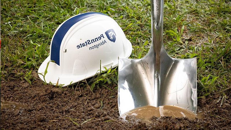 Silver shovel in dirt next to white hard hat with blue letters reading Penn State Abington (near Philadelphia)